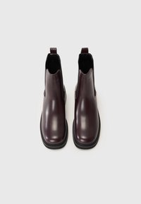 Botas Chelsea de cuero burdeos con un acabado suave, detalles elásticos en los laterales y suelas de goma negras. Presentan un corte bajo en el tobillo y una lengüeta.