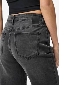 Black denim jeans with a high-rise fit, featuring a patch logo, back pockets, and a slightly faded texture for a modern look.