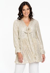 Schimmernde goldene Tunika mit langen Ärmeln, plissiertem Design und Bindegürtel am Ausschnitt. Überzeugt durch reflektierende Pailletten und eine lockere Passform.