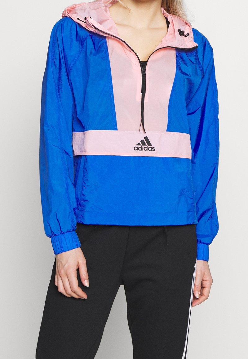 Blå og pink hættetrøje med lynlås i halsen, elastiske manchetter og et broderet logo på brystet. Letvægtsstof.