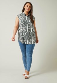 Camicia senza maniche grigia e bianca a fantasia, con bottoni, abbinata a jeans skinny blu e sandali bianchi con zeppa. Tessuto morbido.