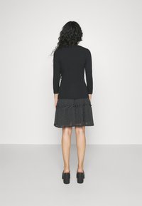 Černý top s dlouhým rukávem a černobílá sukňa s volány a puntíky. Sukňa má rozšířený střih a sahá nad kolena. Černé sandály na podpatku.