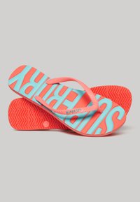 Flip-flops featuring a coral and aqua color scheme, with a textured sole and bold "SUPERDRY" branding on the footbed.