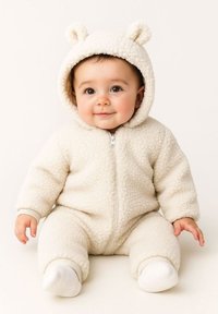 Une combinaison pour bébé en polaire de couleur crème avec une fermeture éclair à l'avant, une capuche dotée d'oreilles d'ours et des poignets côtelés aux poignets et chevilles. Tissu doux et texturé.