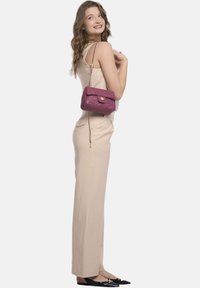 Jumpsuit a coste color beige chiaro, abbinato a una piccola borsa a tracolla bordeaux trapuntata con chiusura dorata e tracolla a catena. Ballerine nere completano il look.