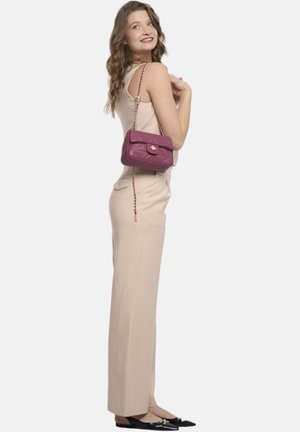Jumpsuit a coste color beige chiaro, abbinato a una piccola borsa a tracolla bordeaux trapuntata con chiusura dorata e tracolla a catena. Ballerine nere completano il look.