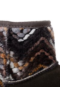 Bota de fieltro marrón con una parte superior tejida texturizada en tonos de gris, marrón y blanco; presenta costuras en contraste a lo largo de los bordes.