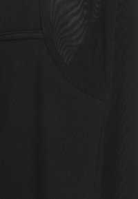 Schwarzes Sporttop aus strukturiertem Stoff mit Mesh-Akzenten auf den Schultern, die eine mehrlagige Optik und ein atmungsaktives Design schaffen.