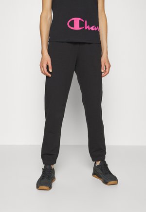 Pantalones de chándal negros con puños elásticos, combinados con una camiseta sin mangas negra que presenta un gran logo rosa. Llevado con zapatillas deportivas negras.
