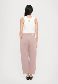Pantalons larges rose clair en tissu lisse avec deux poches arrière. Associé à un haut sans manches blanc affichant un logo dans le dos.