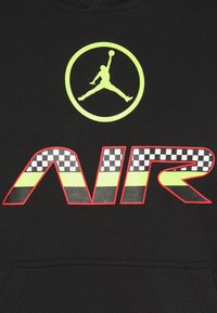 Svart hoodie med en stor neon gul Jumpman-logotyp och texten "AIR" med rutigt mönster och röd kant över bröstet.