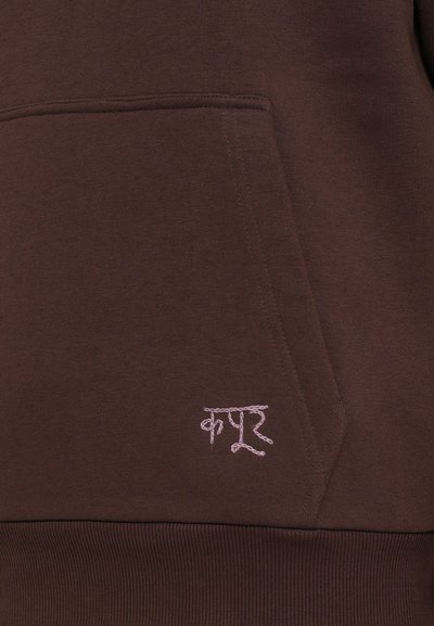 Hanorac maro dintr-un material moale, cu buzunar frontal. Prezintă un text brodat roz în partea stângă jos. Căptușeală ribbed la baza hanoracului.