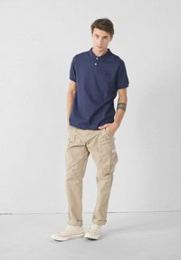 Navy polo shirt met korte mouwen en drie knopen, gecombineerd met beige cargobroek met zijzakken en witte sneakers met een patroon.