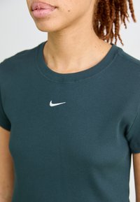 Žalia raukšlėta marškinėliai trumpomis rankovėmis ir su apvalia iškirpte. Yra baltas Nike logotipas siuvinėtas ant krūtinės. Lygus paviršius.