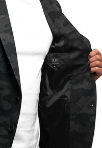 Czarny żakiet kamuflażowy z satynowym podszyciem, z etykieta oznaczoną "JEFF", z zapięciem na guziki oraz eleganckimi detalami wewnętrznej kieszeni.