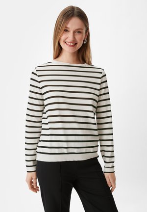 Sweter z długim rękawem w kremowym kolorze w ciemnozielone paski. Miękka tkanina, okrągły dekolt i płaski dół. Noszony z czarnymi spodniami.