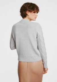 Jasnoszary sweter z dzianiny z ryflowanym dołem i warkoczowym wykończeniem na rękawach. Materiał wydaje się miękki, z luźnym krojem.