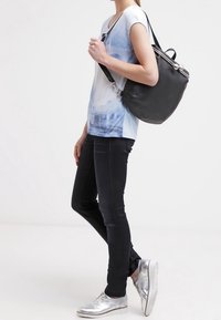 Blå ombre t-shirt, svarta skinny jeans, silverfärgade sneakers och en svart axelväska med metalliska accenter, bärs av en stående figur.