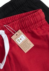 Deux paires de joggings : une noire et une rouge. La paire rouge comporte un cordon blanc et une étiquette indiquant des matériaux écologiques.