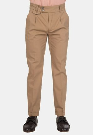 Pantaloni beige da uomo a gamba stretta con vita a doppio bottone, pieghe frontali, orli risvoltati, abbinati a scarpe da cerimonia nere con texture.