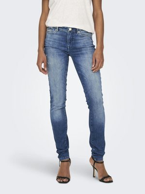 Donna che indossa jeans skinny blu sbiaditi e sandali neri con tacco alto, abbinati a un top bianco senza maniche.