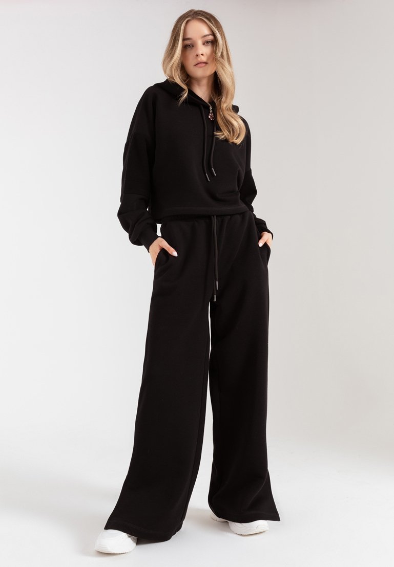 Czarna bluza z kapturem o luźnym kroju z ściągaczem; połączona z luźnymi czarnymi dresami. Białe sneakersy dopełniają casualowy outfit.