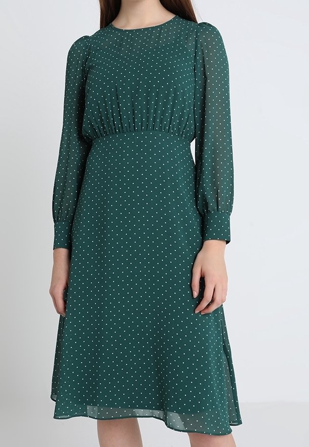 Robe verte à pois en tissu léger, avec des manches longues, une taille froncée et une jupe évasée avec des fentes latérales.