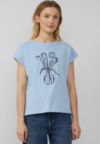 Himmelblaues T-Shirt mit aufgerollten Ärmeln, das ein schwarzes Umrissdesign einer Vase mit fünf Tulpen in der Mitte zeigt. Aus weichem Baumwollstoff.