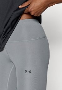 Γκρι αθλητικό κολάν κατασκευασμένο από λείο, ελαστικό ύφασμα, με μαύρο λογότυπο Under Armour και διακριτικές ραφές.