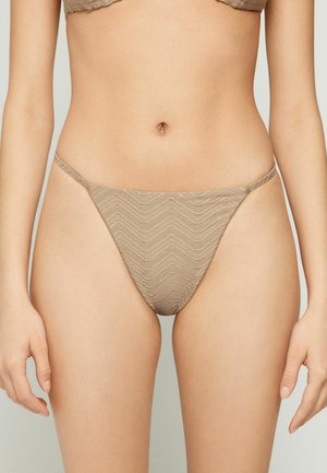 Bas de bikini beige texturé avec jambes échancrées porté par une personne, cadré à la taille et à mi-cuisse, sur fond uni.