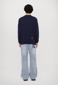 Marineblauer Strickpullover mit gerippten Bündchen und Saum, kombiniert mit hellblauen, übergroßen Denim-Jeans mit gestickten Akzenten und einer lässigen Passform.