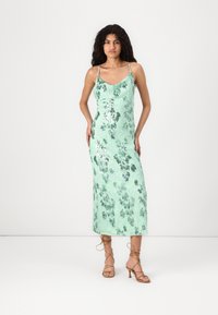 Minzgrünes, ärmelloses Midikleid mit floralem Paillettenmuster, figurbetontem Schnitt und Spaghettiträgern, kombiniert mit nackten Riemchen-Absatzsandalen.