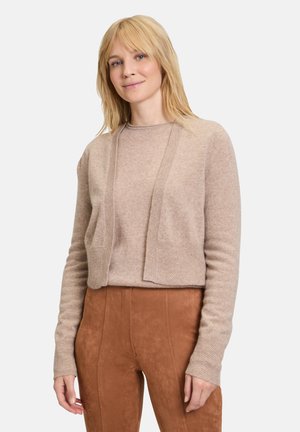 Beige korte cardigan met lange mouwen, in een zachte textuur. Gestyled met bijpassende bruine aansluitende broek, met een gladde afwerking.