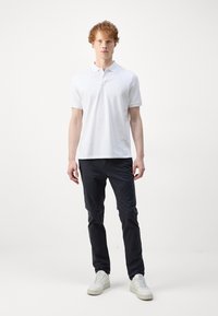 Witte poloshirt met kraag, gecombineerd met donkere broek en witte sneakers. De stof lijkt glad en de pasvorm is casual.