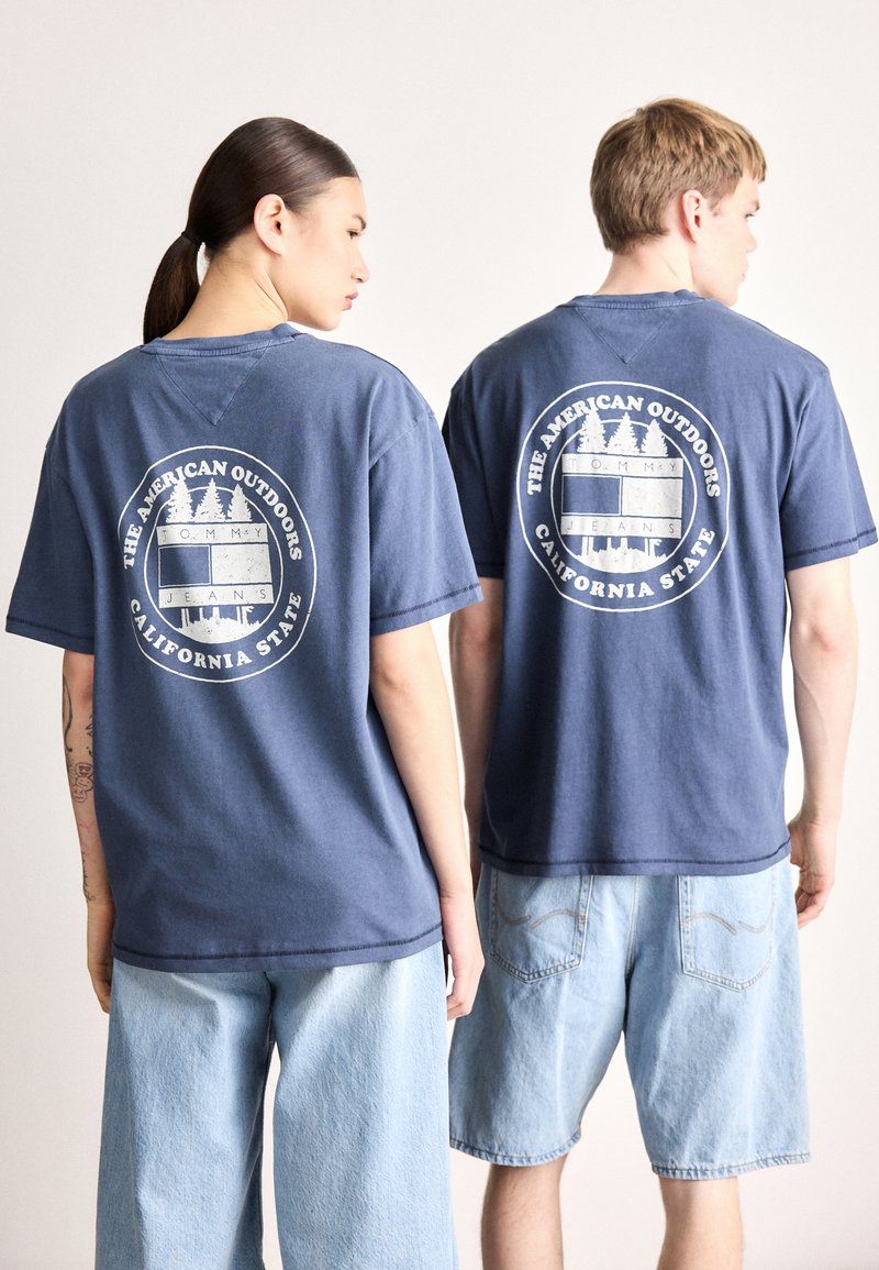 Tamsiai mėlyni medvilniniai marškinėliai su apskritu grafiniu atspaudu nugaroje, vaizduojančiu medžius ir užrašu "California State", derinami su šviesiai mėlynomis džinsinėmis šortais.