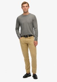 Graues langärmliges Shirt, khakifarbene Hose und schwarze Schuhe. Das Shirt hat einen Rundhalsausschnitt, und die Hose hat einen geraden Schnitt mit einer strukturierten Oberfläche.