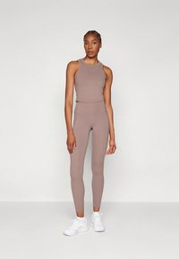 Brun sömlös linne kombinerad med matchande högmidjade leggings. Modellen bär vita träningsskor. Mjuk textur och figurnära design.