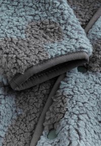 Textura difusa en diferentes tonalidades de azul y gris, con un borde oscuro suave y costuras visibles, mostrando un diseño superpuesto.