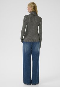 Maglione grigio a collo alto con una silhouette aderente abbinato a jeans larghi in denim azzurro chiaro. Texture liscia e strisce verticali.