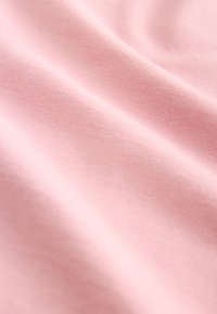 Blødt lyserødt bomuldsstof med en glat overflade, der har en svag glans og subtil tekstur, draperet i bløde folder.