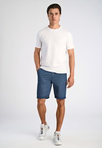 Maglietta bianca a maniche corte abbinata a pantaloni corti a scacchi blu navy, con risvolti alle maniche, e scarpe da ginnastica bianche con accenti colorati.