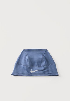 Bonnet bleu Nike de style beanie avec panneaux cousus et logo blanc Swoosh à l'avant, présenté sur un fond clair uni.