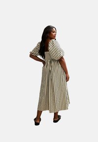 Gestreiftes Midi-Kleid in Creme und Schwarz, mit Puffärmeln, tailliertem Schnitt und offenem Rücken. Getragen mit schwarzen flachen Schuhen.