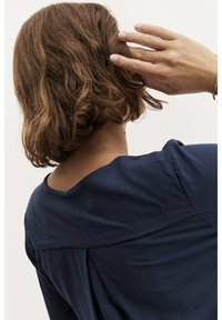 Mörkblå blus med rundad halsringning, mjuk textur och veckdetalj bak, med korta ärmar och en avslappnad passform.