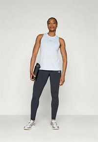 Ljusblå ärmlös atletisk topp, åtsittande mörkgrå tights och sneakers. Håller en svart vattenflaska. Enkel, sportig design.