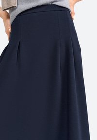Jupe plissée marine en tissu texturé, dotée d'une taille lisse et d'un design fluide, adaptée à diverses occasions.