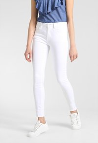 Jeans skinny bianchi in denim con vestibilità regolare, caratterizzati da cinque tasche, chiusura con bottone e leggero stretch per il comfort. Abbinati a sneakers bianche.