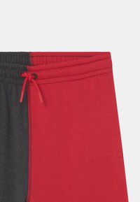 Czerwone i szare spodnie dresowe z elastycznym pasem, wyposażone w sznurek oraz kontrastowe panele. Gładka faktura i lekki materiał.