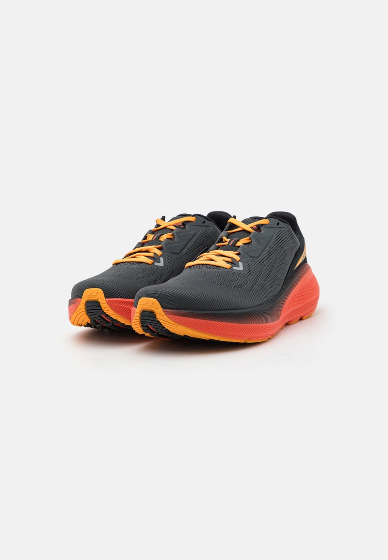 Zapatillas deportivas con parte superior de malla negra, cordones naranjas y acentos en la suela. Suela exterior de goma negra texturizada con detalles vibrantes en naranja y rojo.