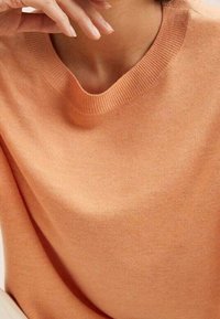 Maglione a maglia arancione chiaro con collo a girocollo a coste, texture morbida e vestibilità rilassata, che mette in risalto una superficie del tessuto liscia ed uniforme.